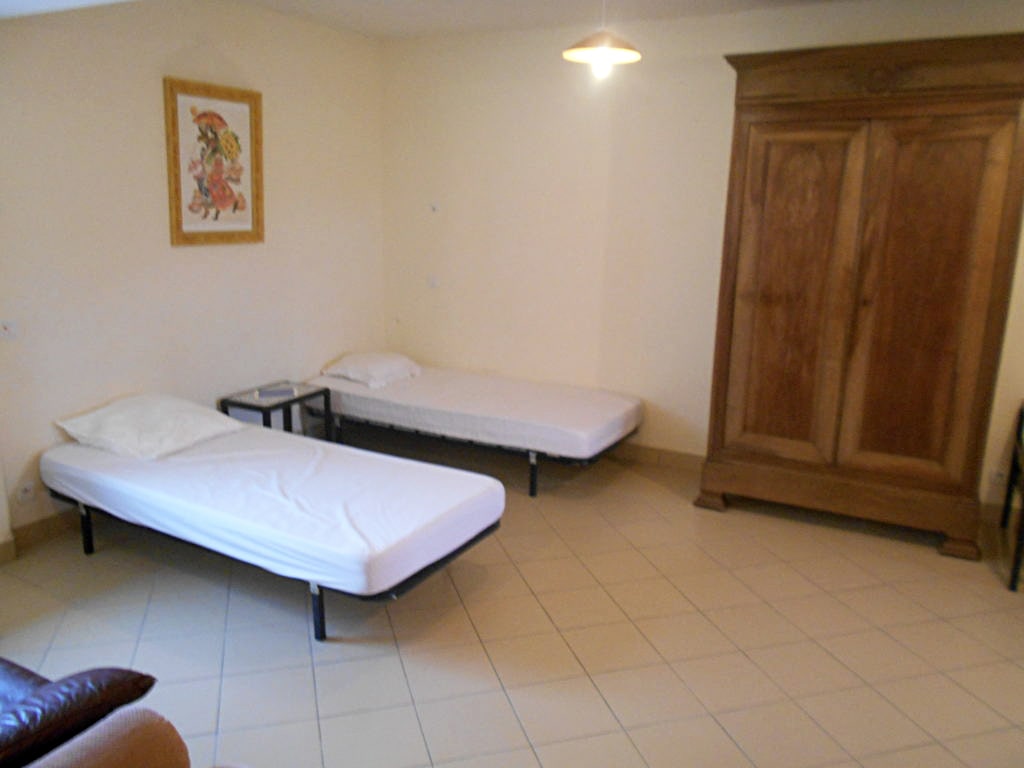 photo d'une chambre, avec deux lits simples, murs blanc, une grande armoire en bois, une table de chevet, fauteuil en cuir marron, du gîte de groupe et maison d'hôtes du Bas Mena