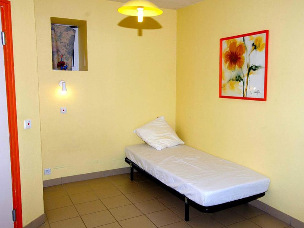 photo d'une chambre, avec un lit simple, murs jaune clair, une petite fenêtre avec rideau, du gîte de groupe et maison d'hôtes du Bas Mena
