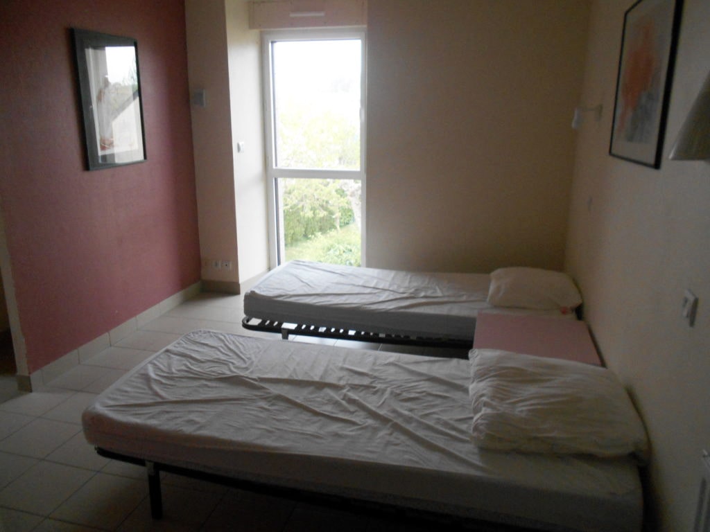 photo d'une chambre, avec deux lits simples, une table de chevet rose, mur beige et mur rose, fenêtre de plain pied, du gîte de groupe et maison d'hôtes du Bas Mena
