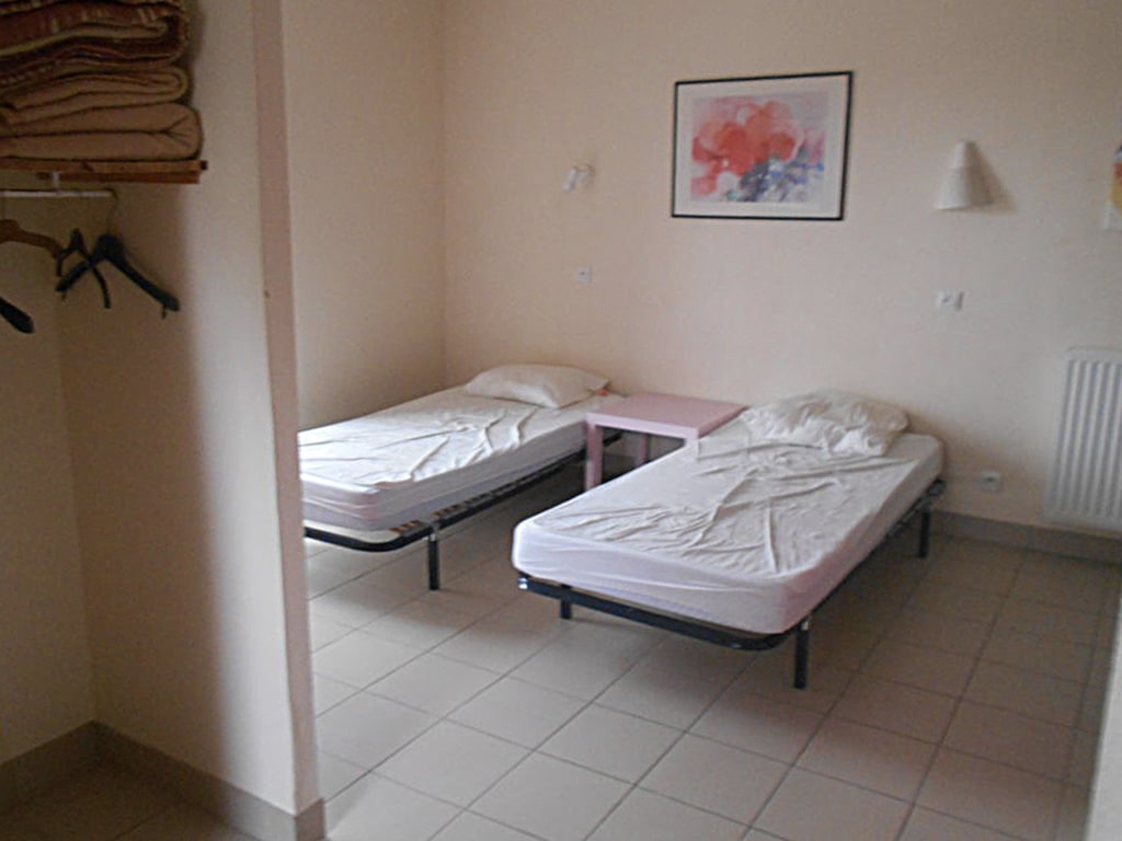 photo d'une chambre, avec deux lits simples, une table de chevet rose, mur beige, radiateur, penderie, du gîte de groupe et maison d'hôtes du Bas Mena
