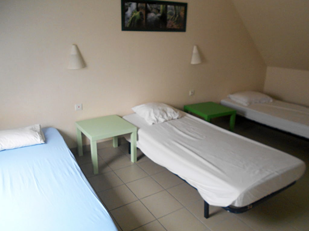 photo d'une chambre sous les toits, avec trois lits simples, deux tables de chevet verte, mur beige, du gîte de groupe et maison d'hôtes du Bas Mena
