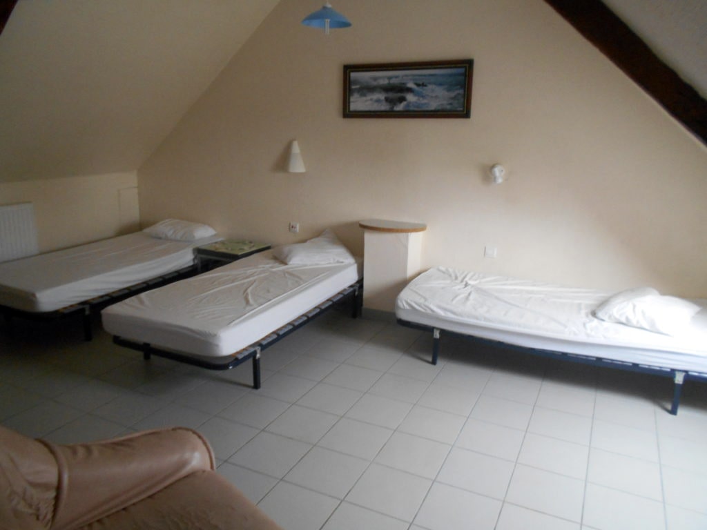 photo d'une chambre sous les toits, avec trois lits simples, deux tables de chevet, mur beige avec poutre apparente, fauteuil beige, radiateur, du gîte de groupe et maison d'hôtes du Bas Mena