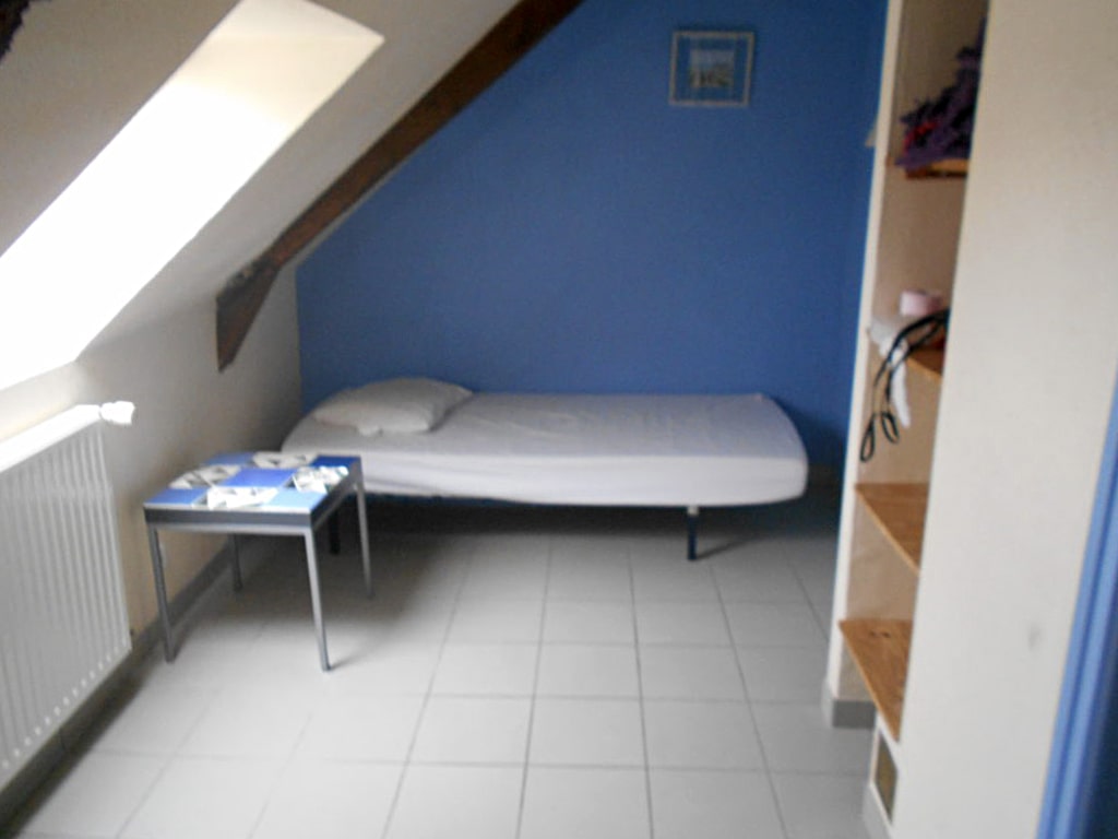 photo d'une chambre, avec un lit simple, table de chevet, mur bleu et mur blanc avec poutre apparente, radiateur et étagères murale et lucarne de toit, du gîte de groupe et maison d'hôtes du Bas Mena