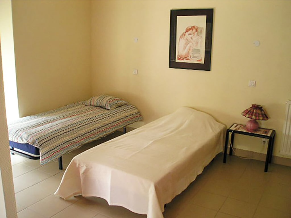 photo d'une chambre, avec deux lits simples, table de chevet et sa lampe, mur beige, du gîte de groupe et maison d'hôtes du Bas Mena