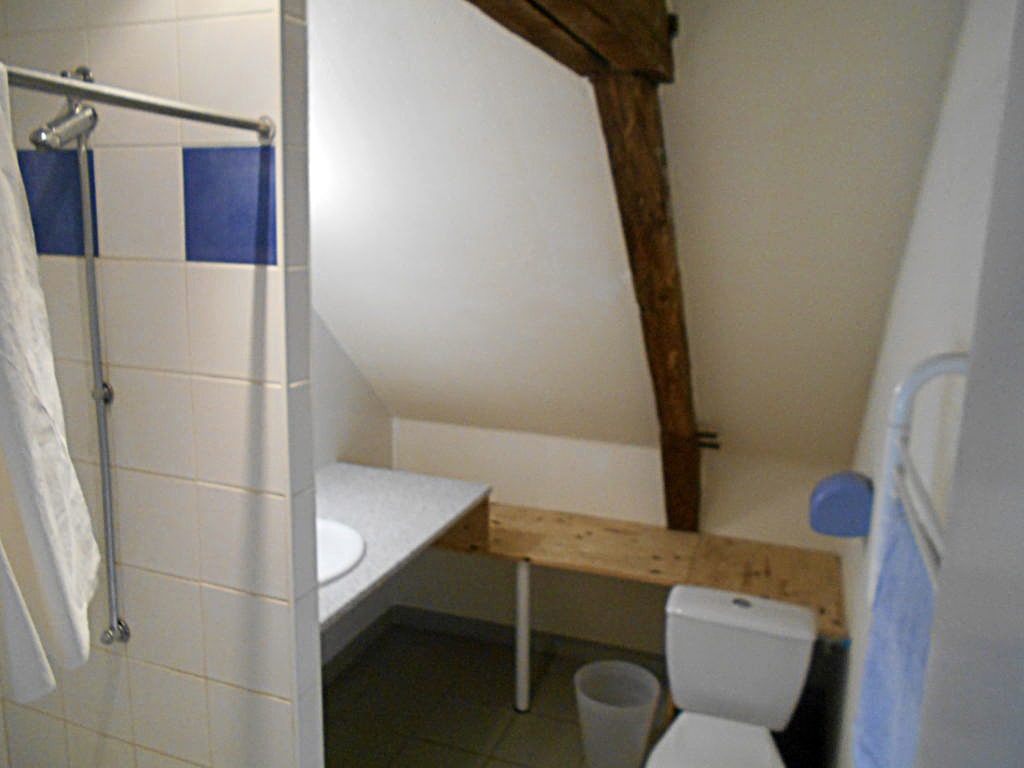 photo d'une sale de bain sous les toits, carreaux blanc avec frise de carreaux bleu, lavabo, toilette, porte serviette, poutres apparentes, du gîte de groupe et maison d'hôtes du Bas Mena
