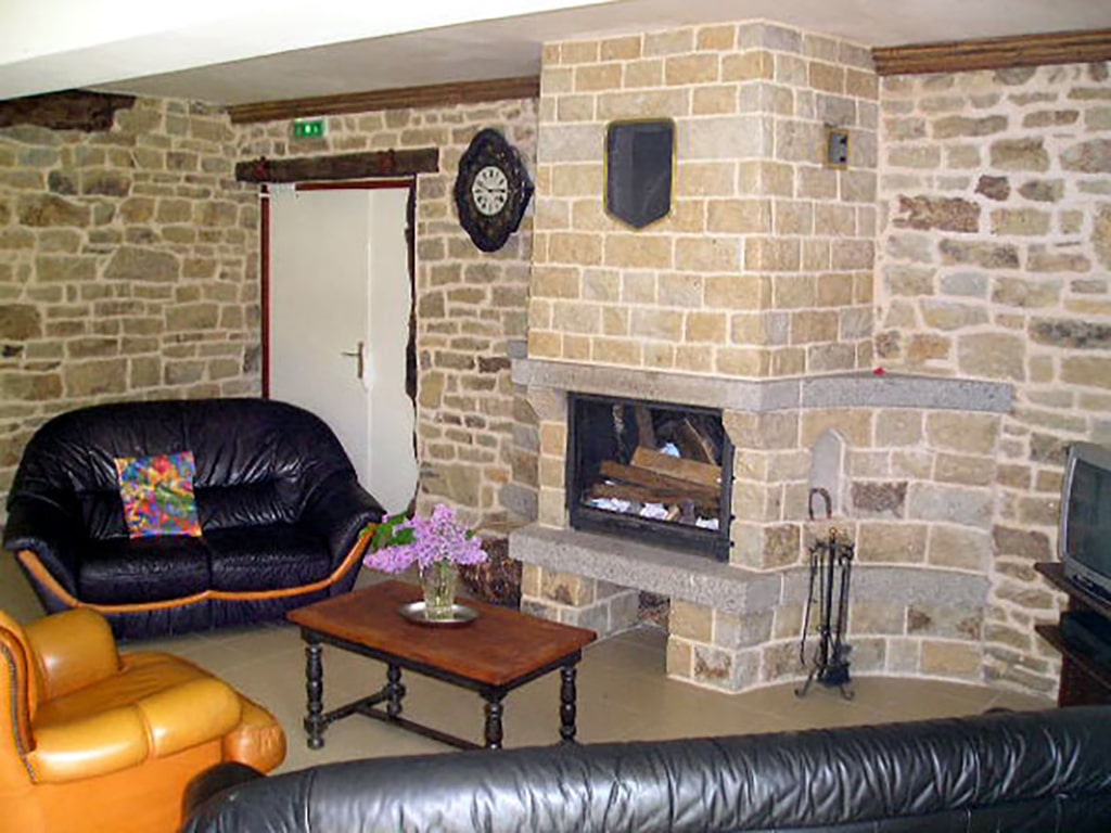 photo d'un salon avec cheminée, deux canapés en cuir noir, un fauteuil en cuir couleur caramel, table basse, télévision, murs en pierre, du gîte de groupe et maison d'hôtes du Bas Mena