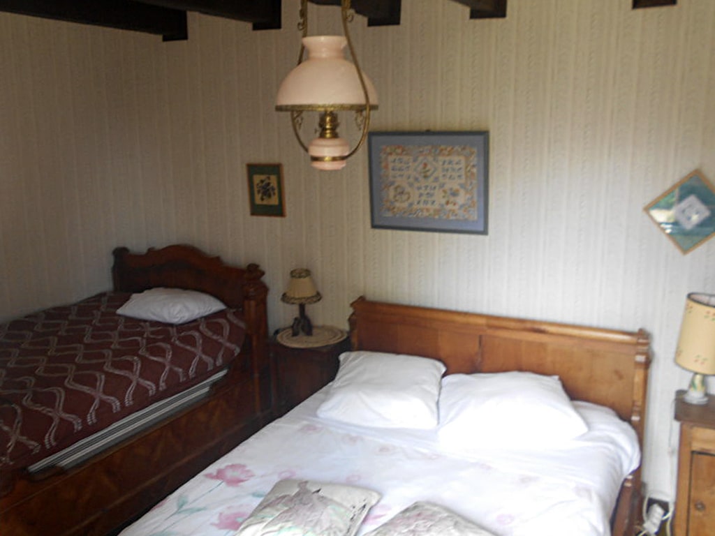photo d'une chambre avec un lit double et un lit simple, petites tables de chevet et leurs lampes, chandelier, armoire en bois, du gîte de groupe et maison d'hôtes du Bas Mena