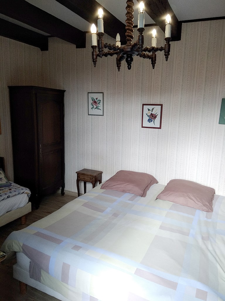 photo d'une chambre avec un lit double, petite table de chevet, chandelier, armoire en bois, du gîte de groupe et maison d'hôtes du Bas Mena