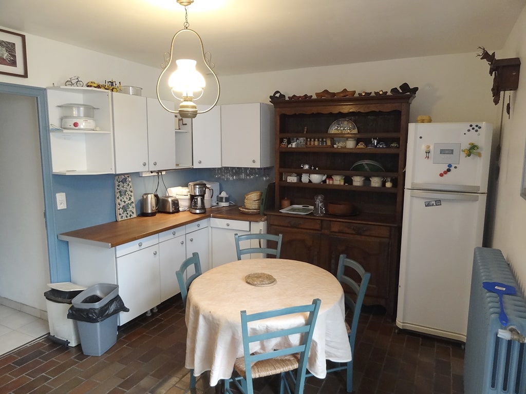 photo d'une cuisine, placards murale et plan de travail, frigidaire avec congélateur, une table et quatre chaises, vaisselier, horloge coucou en bois, du gîte de groupe et maison d'hôtes du Bas Mena