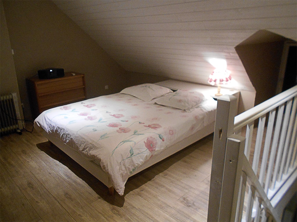 photo d'un lit double dans un chambre sous les toits, lampe de chevet, montée d'escalier et lucarne de toit, du gîte de groupe et maison d'hôtes du Bas Mena