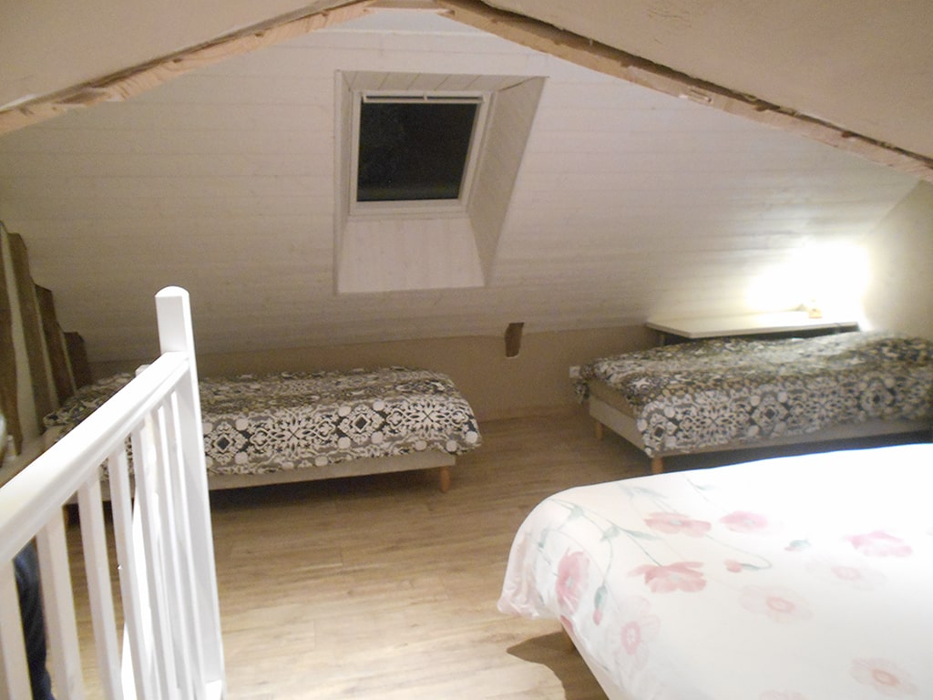 photo d'une chambre avec deux lits simples et un lit double sous les toits, poutres apparentes et lucarne de toit et montée d'escalier, du gîte de groupe et maison d'hôtes du Bas Mena